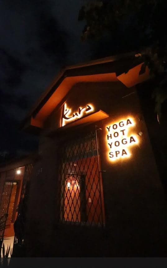 Fachada do Kura à noite com o letreiro iluminado de yoga, hot yoga e spa